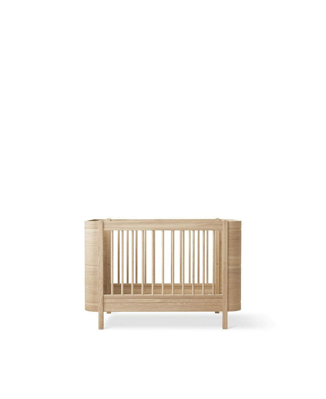 Wood Mini+ Babybett aus weiß geölter massiver Eiche mit höhenverstellbarem Lattenrost und abnehmbaren Gitterstäben, skandinavisches Design für Babys bis 3 Jahre.